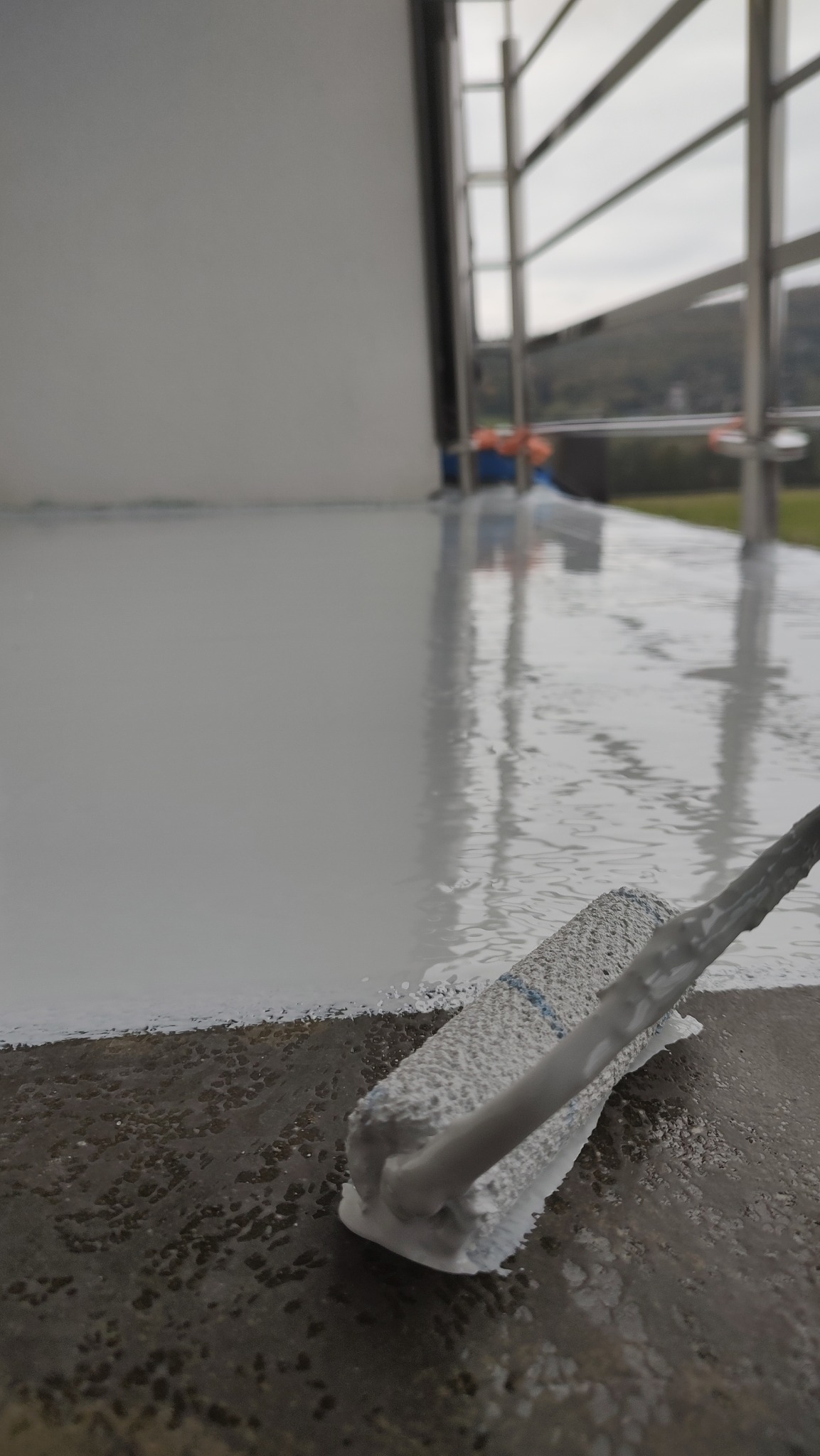 Malowanie podłogi balkonu wałkiem w Łętowni, widok na świeżo nałożoną, błyszczącą warstwę w jasnym kolorze.