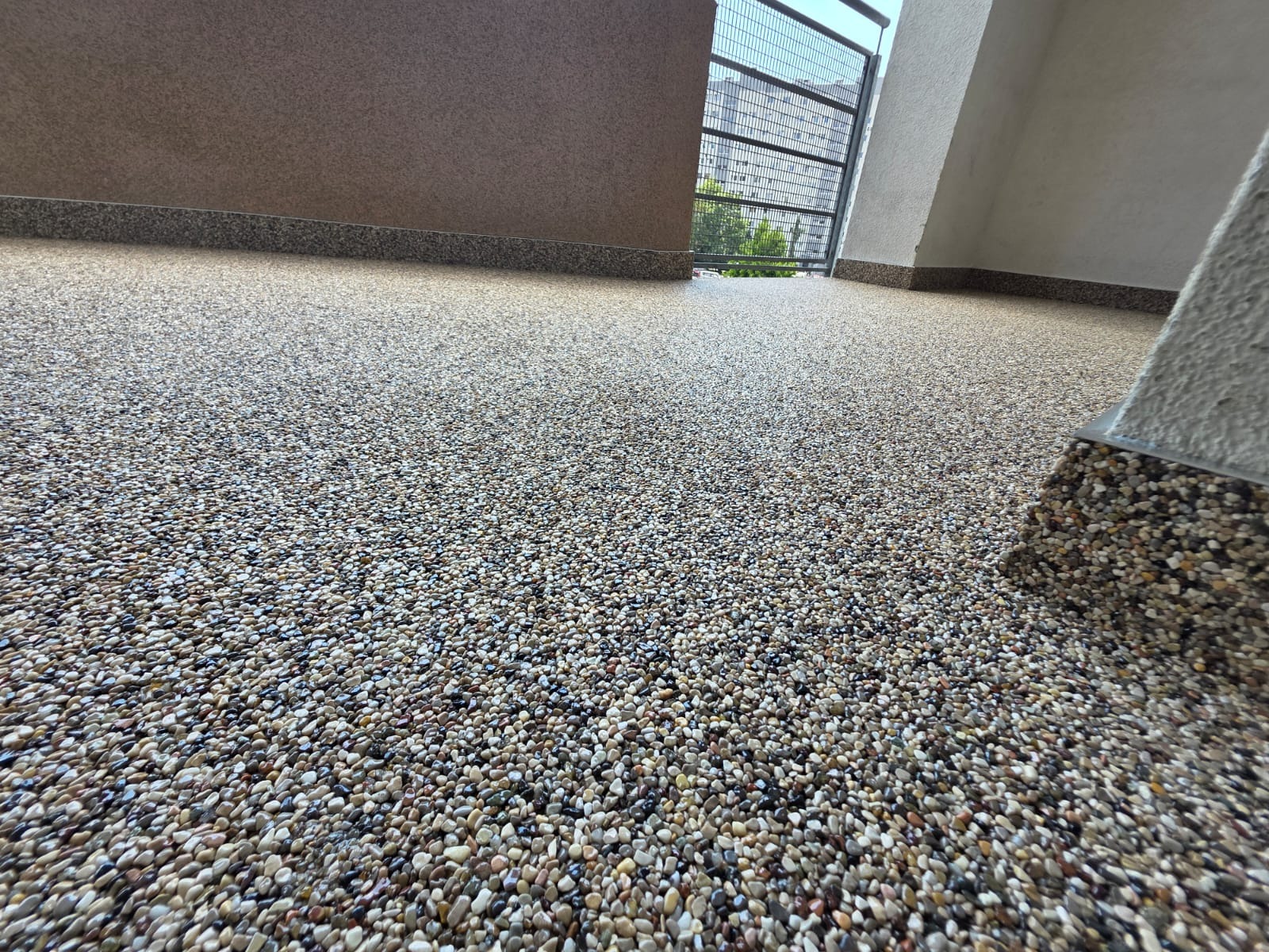 Balkon z wykończeniem z drobnych kamyczków w odcieniach szarości i beżu, widok z niskiej perspektywy, z fragmentem balustrady w tle.