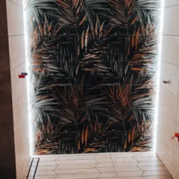 Wykończona łazienka z kabiną prysznicową typu walk-in, wyłożoną płytkami z motywem liści palmowych i podświetleniem LED, drewnopodobna podłoga z odpływem liniowym.