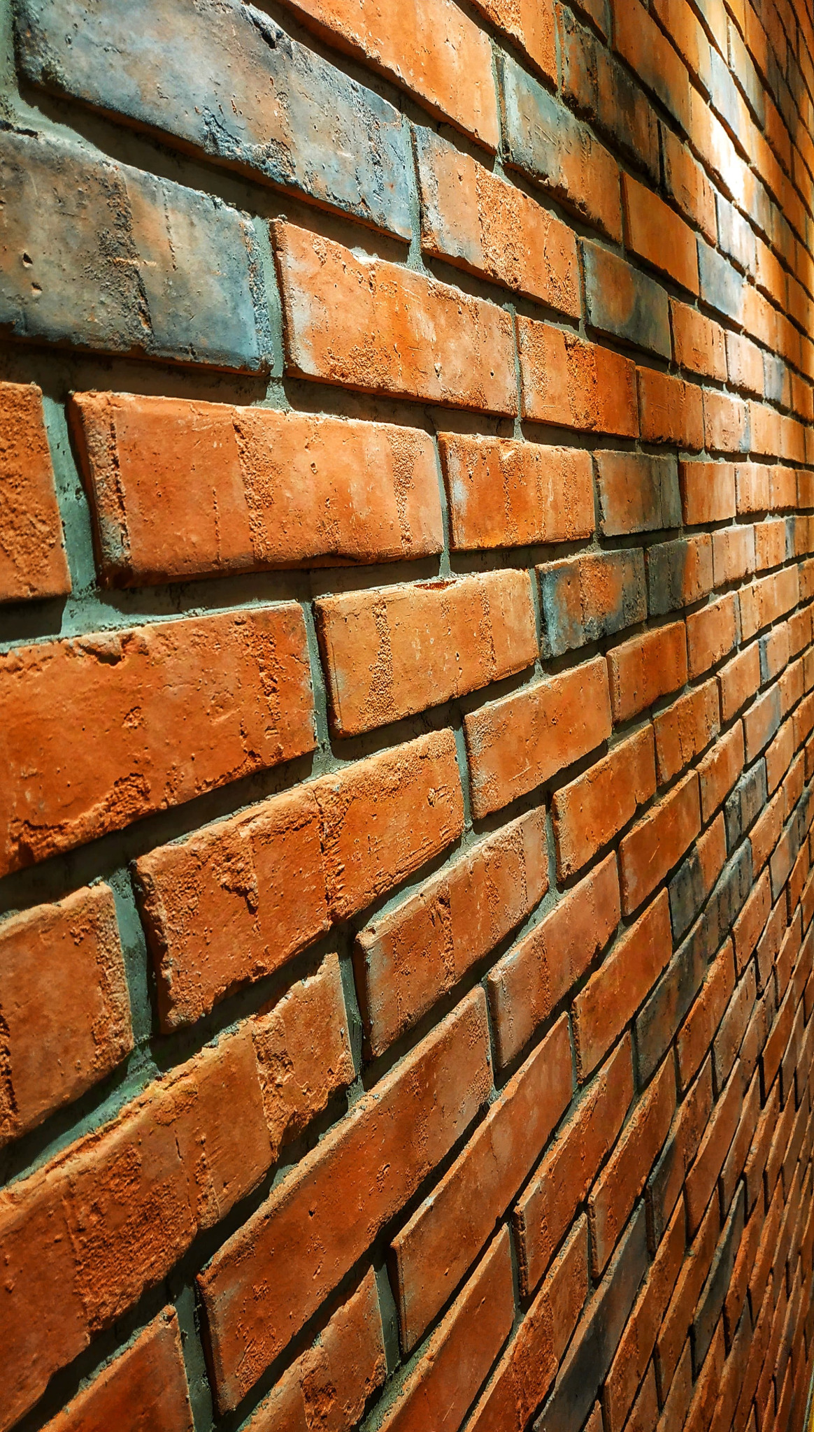 Ściana z cegły klinkierowej w odcieniach czerwieni i szarości, ułożona pod kątem, z widoczną fakturą i fugami.