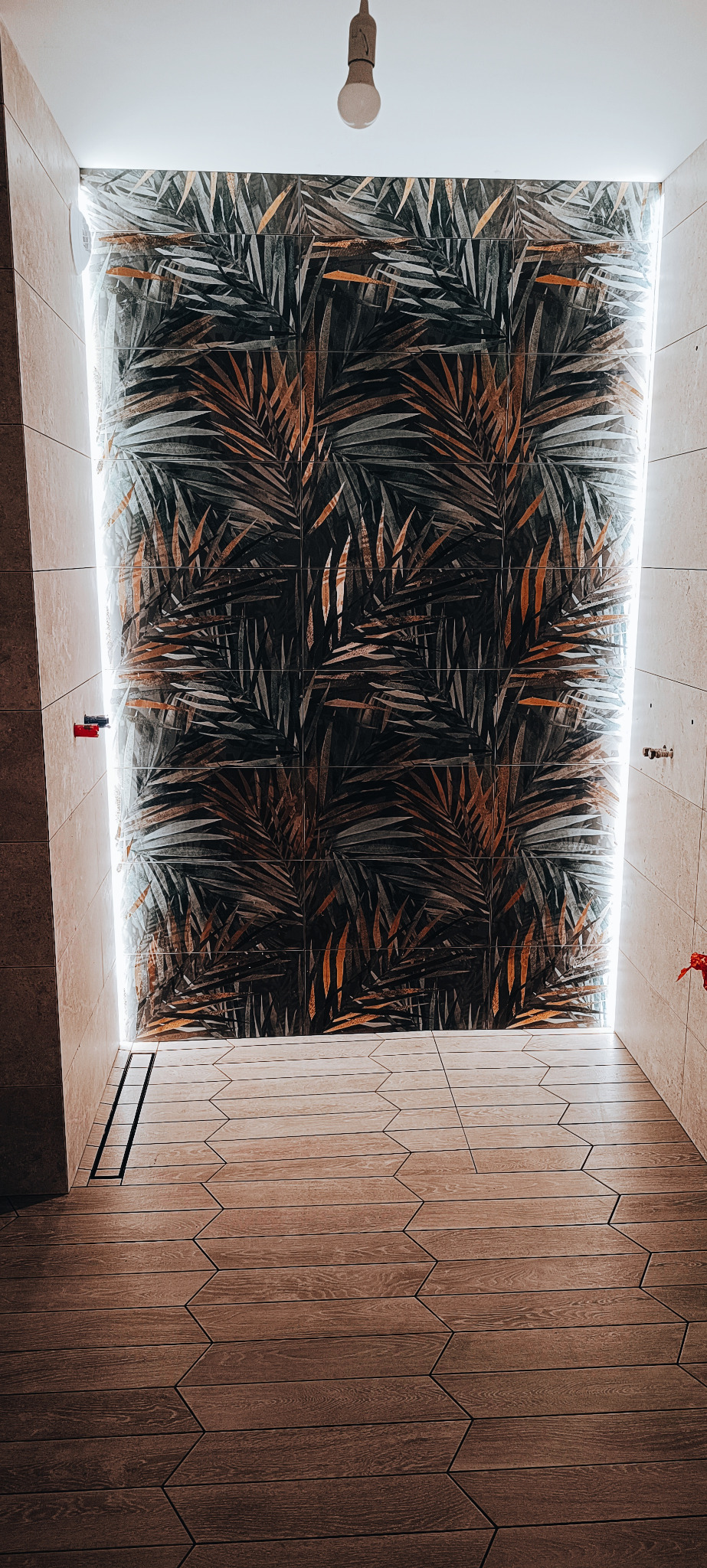 Wykończona łazienka z kabiną prysznicową typu walk-in, wyłożoną płytkami z motywem liści palmowych i podświetleniem LED, drewnopodobna podłoga z odpływem liniowym.