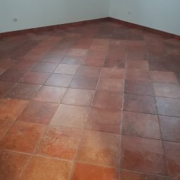 ALL-BUD Arkadiusz Bednarek - Ułożona terakota w odcieniach brązu i pomarańczy, widoczne gniazdka elektryczne przy podłodze, ściany pomalowane na biało.