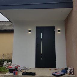 ALL-BUD Arkadiusz Bednarek - Nowoczesne wejście do domu z czarnymi drzwiami, oświetleniem zewnętrznym i narzędziami na schodach.