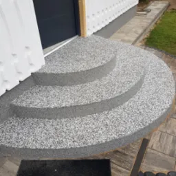 Wykończenie schodów wejściowych żywicą epoksydową w odcieniach szarości, z widoczną strukturą kamyczkową. Nowoczesne rozwiązanie, estetyczne i trwałe.