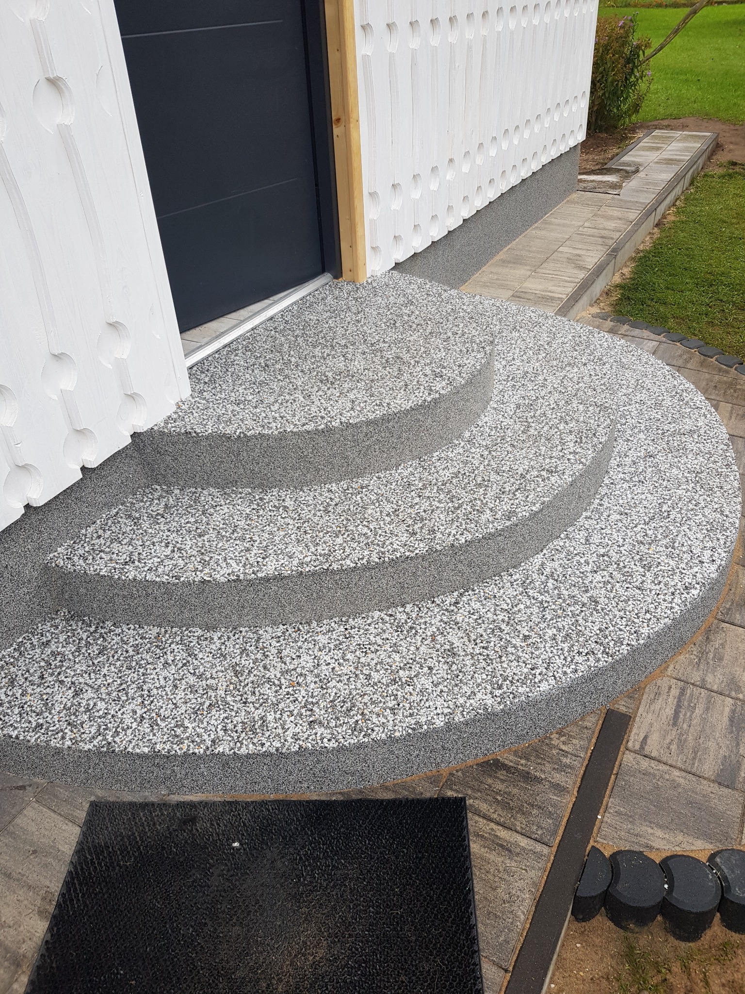 Wykończenie schodów wejściowych żywicą epoksydową w odcieniach szarości, z widoczną strukturą kamyczkową. Nowoczesne rozwiązanie, estetyczne i trwałe.