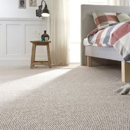 FloorArt - Jasna wykładzina dywanowa w sypialni z łóżkiem i stolikiem nocnym. Delikatne światło dzienne podkreśla teksturę dywanu, tworząc przytulną atmosferę.