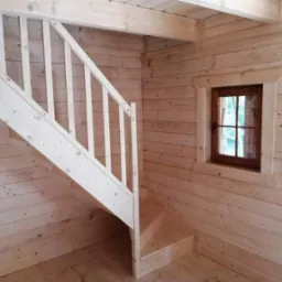 Wnętrze drewnianego domu szkieletowego z jasnymi schodami i oknem z drewnianą ramą.