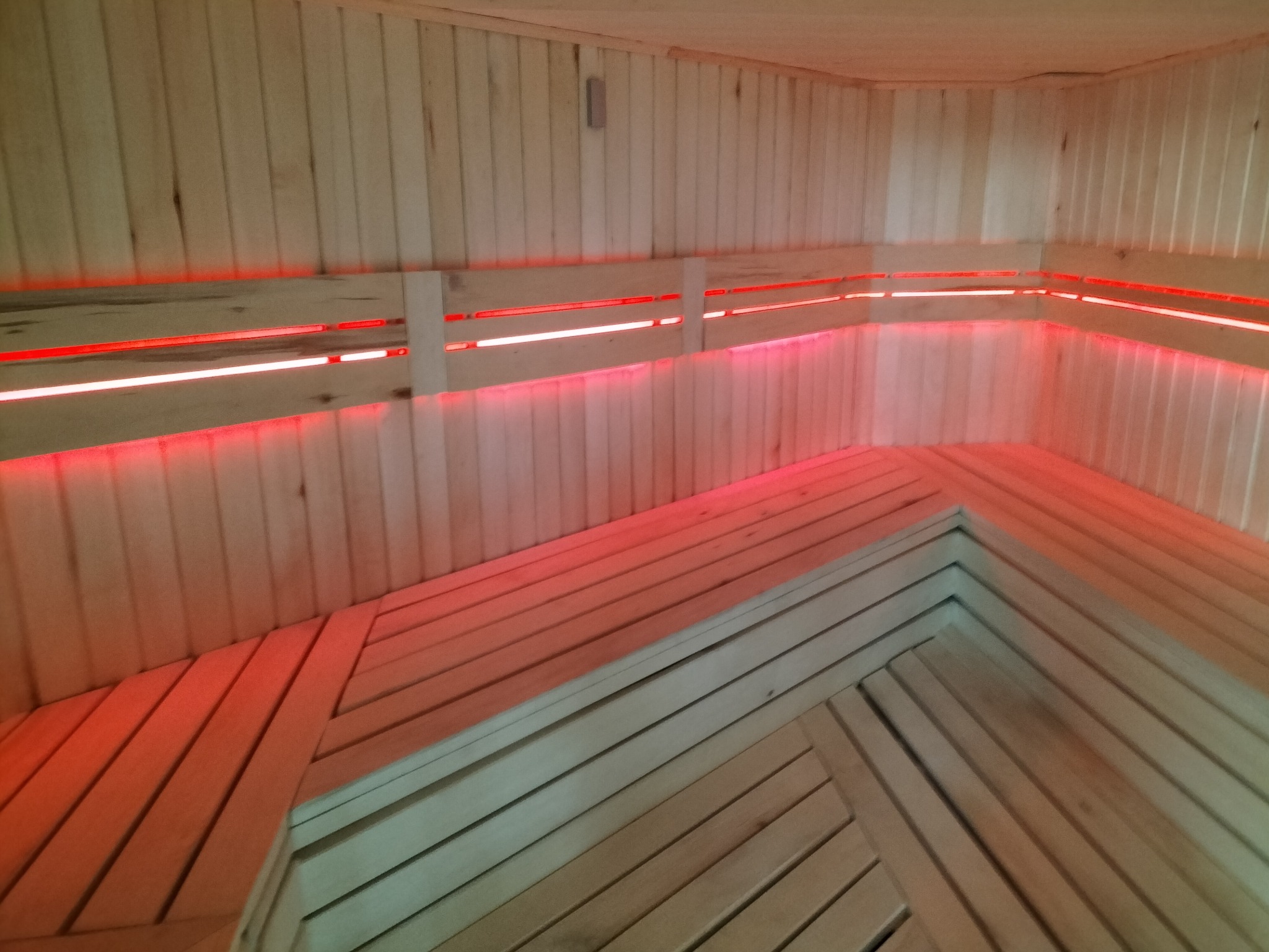 Wnętrze sauny wyłożone jasnym drewnem, z podświetleniem LED w kolorze czerwonym, oświetlającym ławki i ściany.