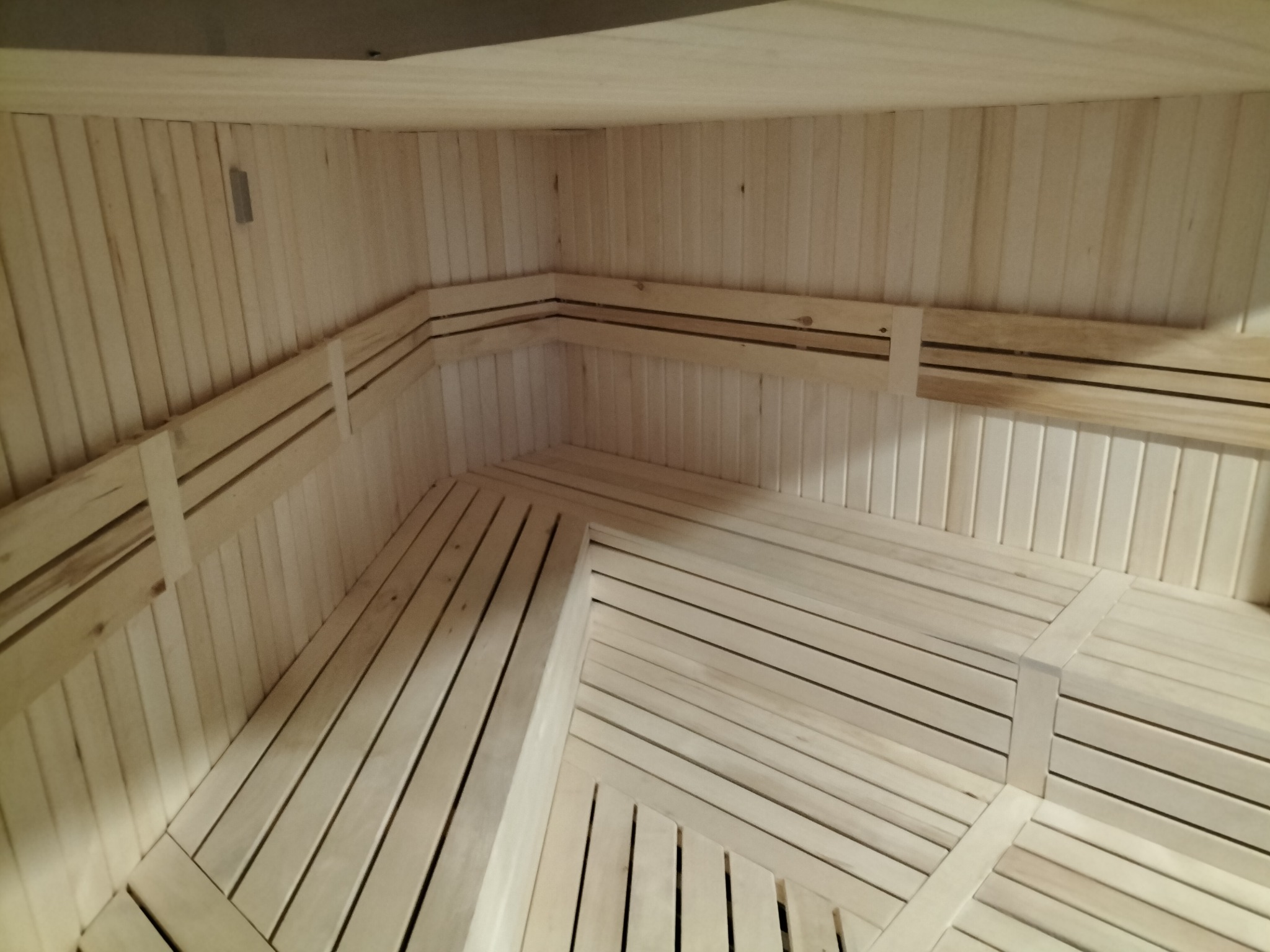 Wnętrze sauny wykończone jasnym drewnem, z widocznymi ławkami i panelami ściennymi, oświetlenie punktowe na górze.