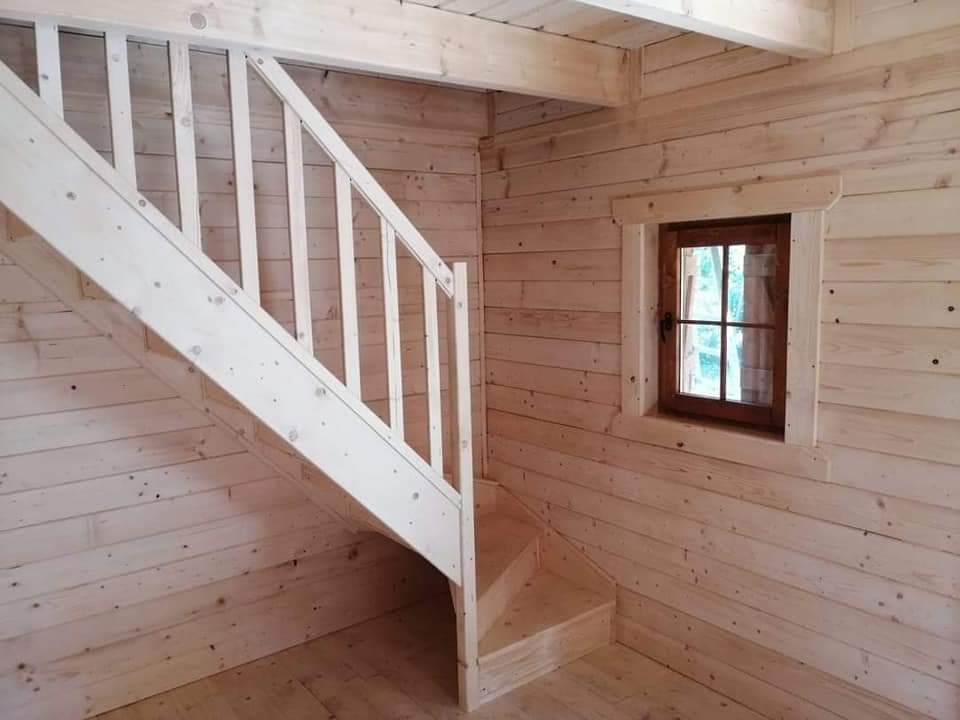 Wnętrze drewnianego domu szkieletowego z jasnymi schodami i oknem z drewnianą ramą.
