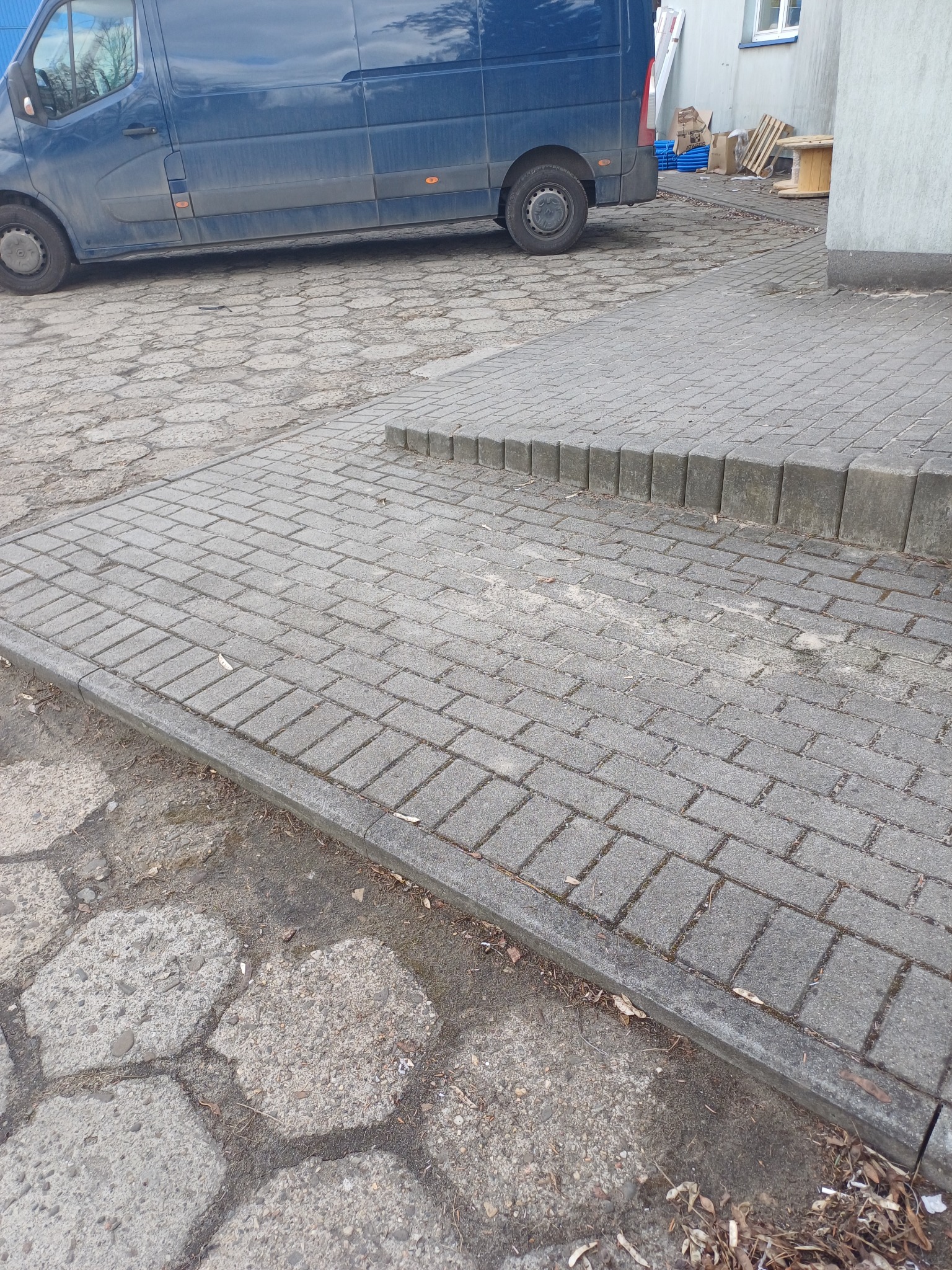 Brudny, niebieski samochód dostawczy zaparkowany na szarej kostce brukowej z widocznymi śladami zabrudzeń i mchu.