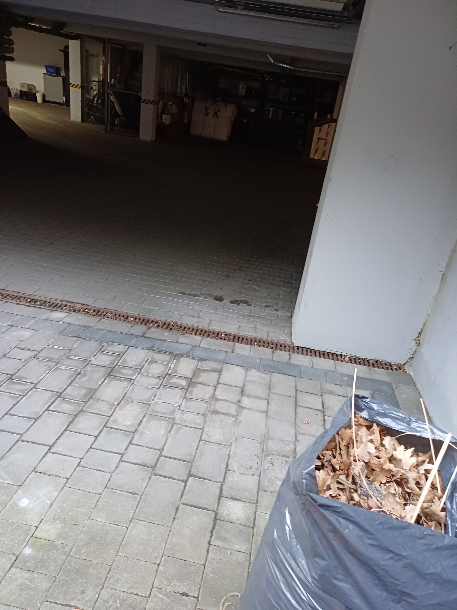 Worek na liście stojący na kostce brukowej przy ścianie budynku z widoczną kratką ściekową.