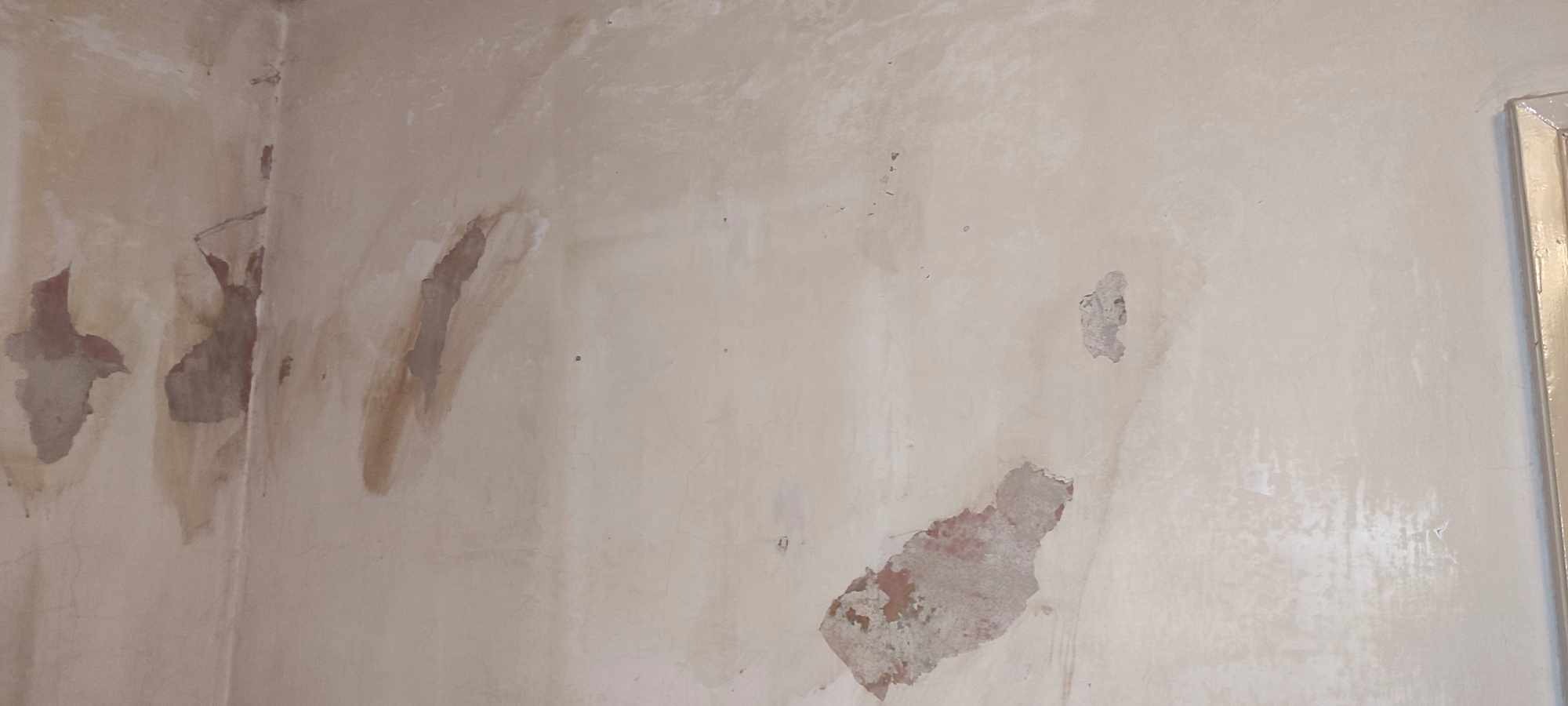 Ściana w rogu pomieszczenia z widocznymi ubytkami tynku i śladami po zalaniach, przygotowana do dalszych prac wykończeniowych.