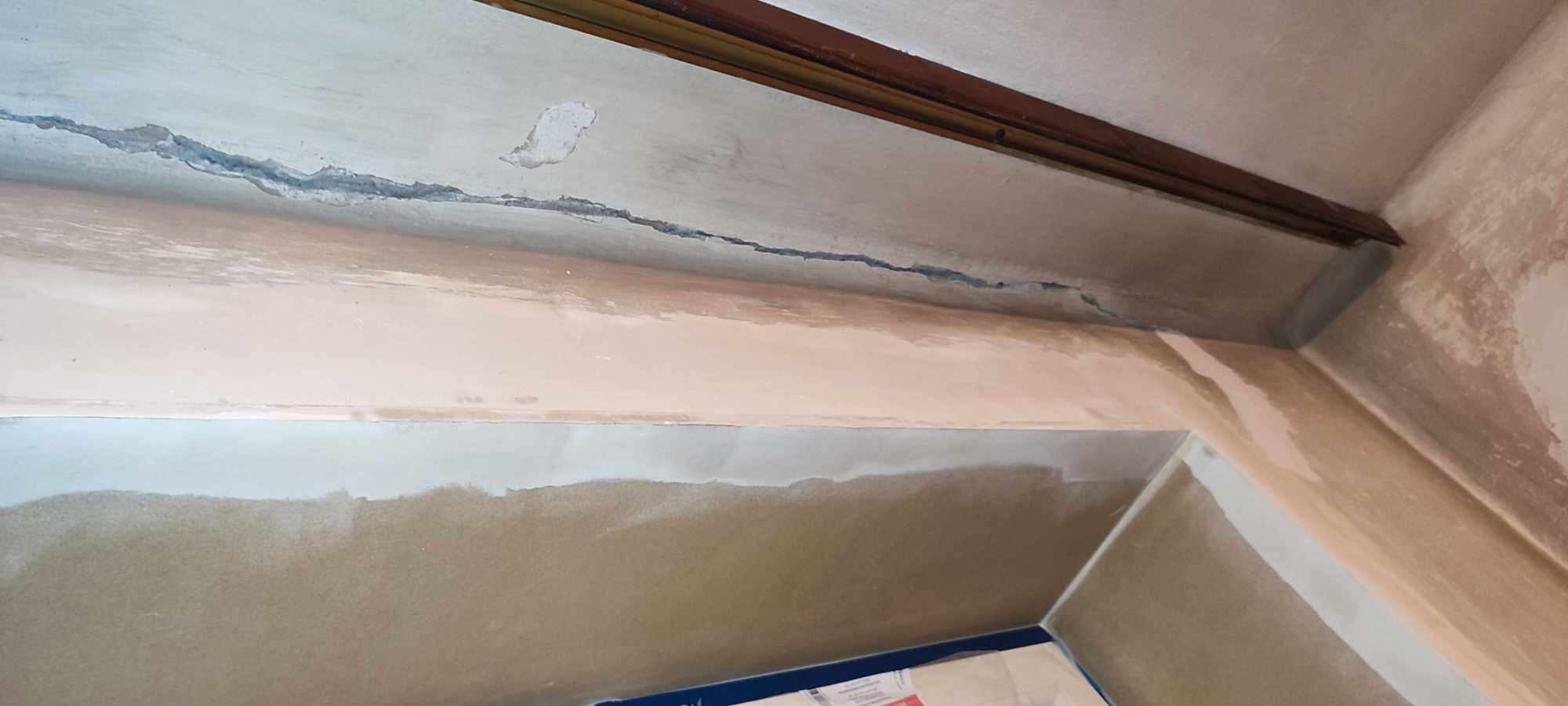 Niedokończona ściana i sufit w trakcie prac wykończeniowych, widoczne pęknięcia i warstwy gładzi gipsowej, przygotowanie do malowania.