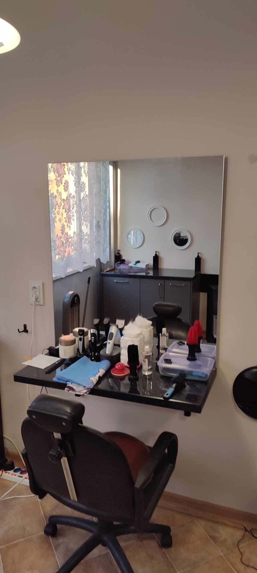 Stanowisko fryzjerskie z lustrem, różnymi narzędziami i akcesoriami do strzyżenia i stylizacji włosów, widoczne krzesło fryzjerskie.