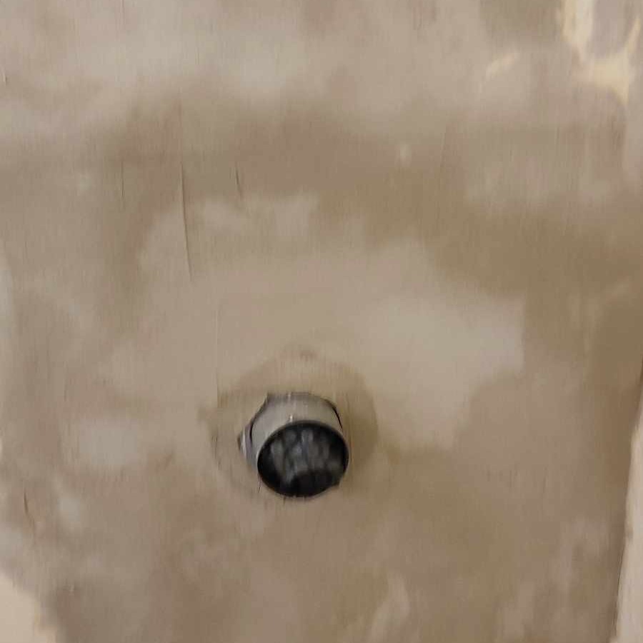 Ściana w trakcie szpachlowania, z wystającym fragmentem instalacji elektrycznej w metalowej puszce, widoczne nierówności i ślady po szpachli.