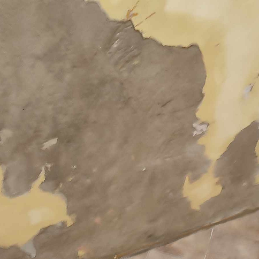 Zniszczona, odchodząca farba na ścianie w Czechowicach-Dziedzicach, ukazująca szary podkład i fragmenty żółtej farby wierzchniej.