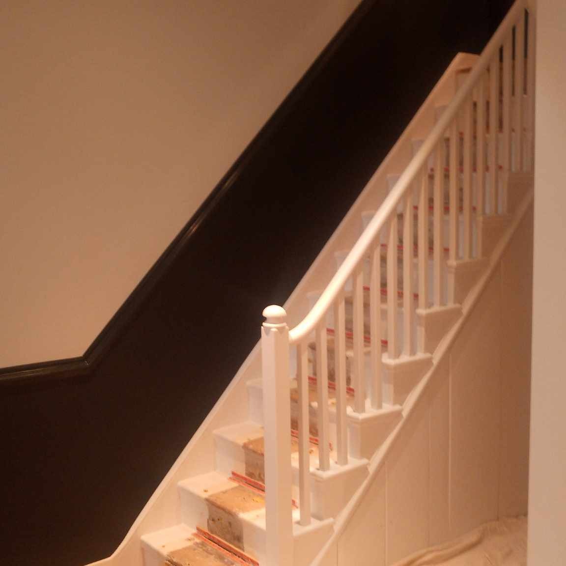 Klatka schodowa w trakcie malowania: białe balustrady i schody z zabezpieczeniami, ciemna ściana wzdłuż biegu schodów.