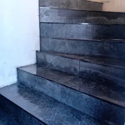 Wykończone, ciemne schody z płytek w Ostrowi Mazowieckiej. Widoczne detale fug i krawędzi. Ściana częściowo przygotowana do malowania.