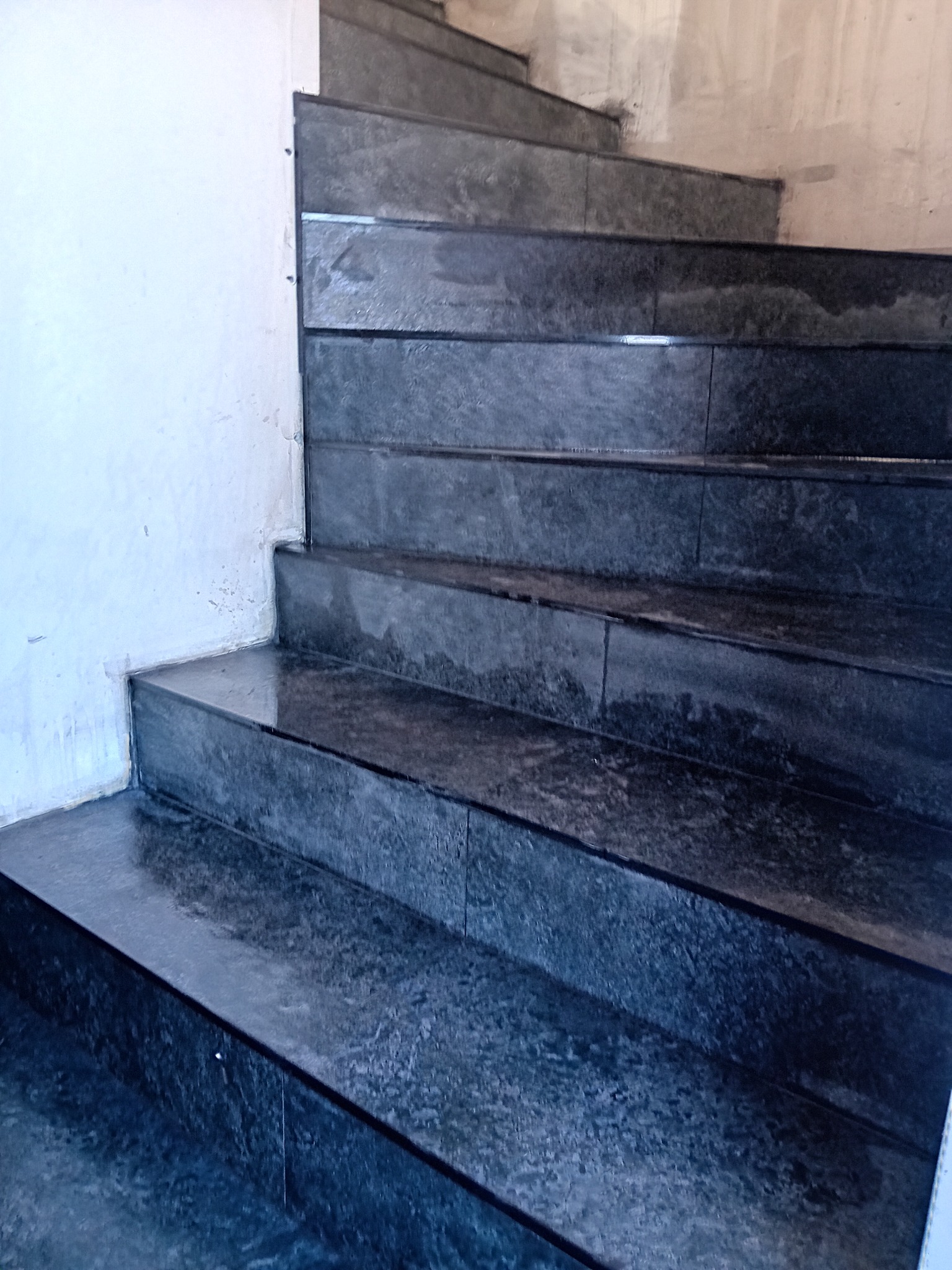 Wykończone, ciemne schody z płytek w Ostrowi Mazowieckiej. Widoczne detale fug i krawędzi. Ściana częściowo przygotowana do malowania.