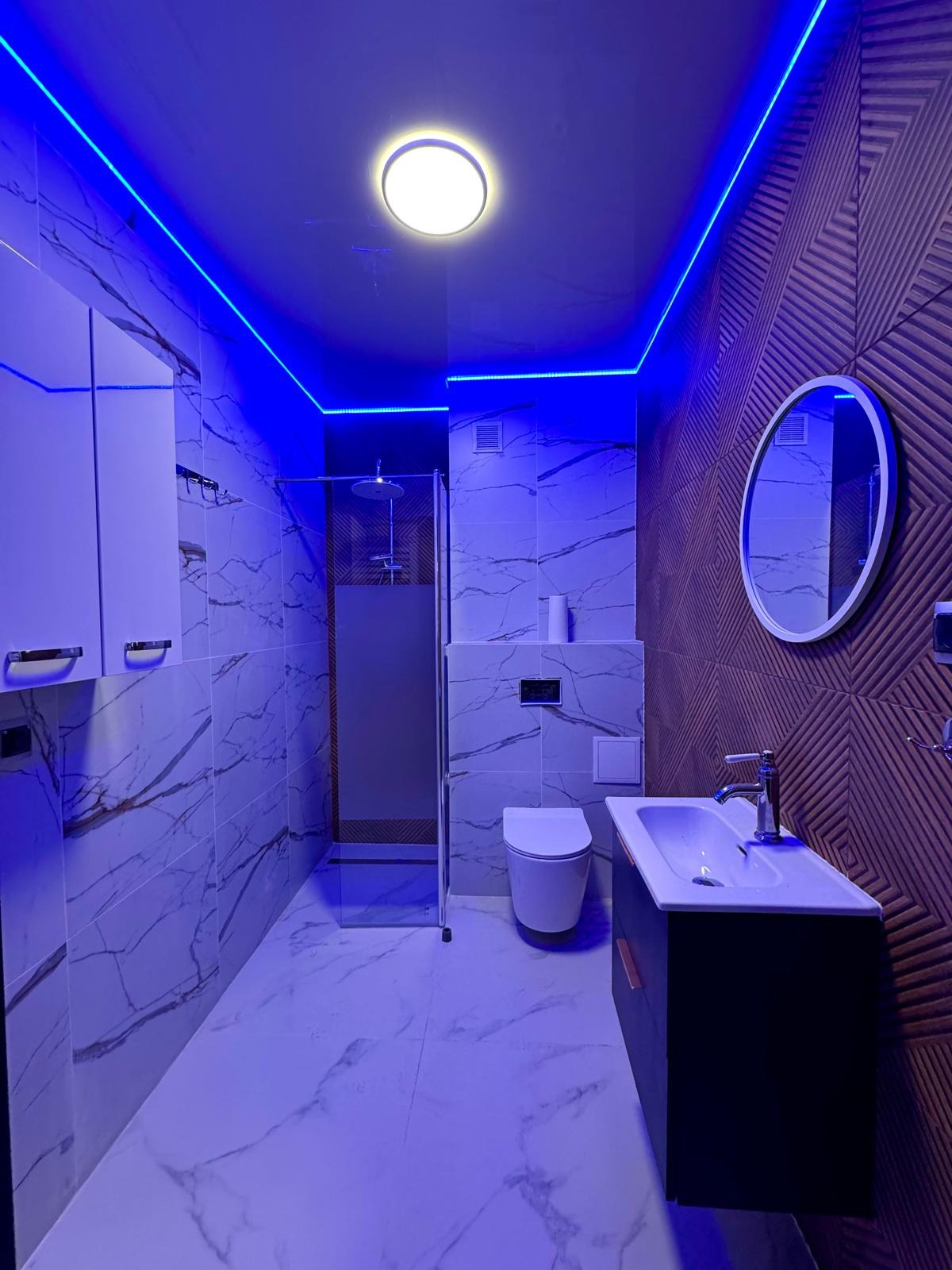 Nowoczesna łazienka z marmurowymi płytkami, podświetleniem LED i geometryczną ścianą akcentującą