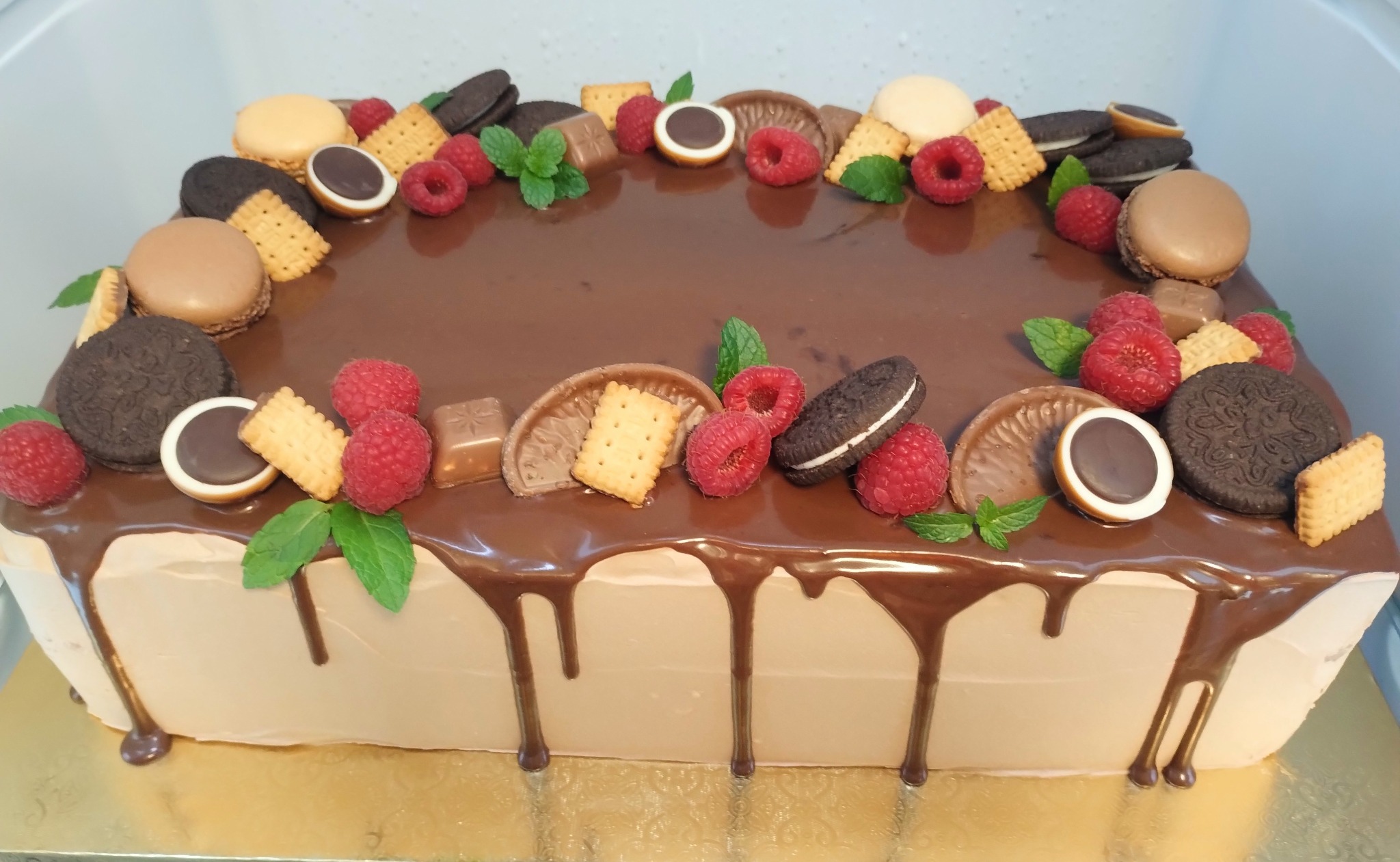 Prostokątny tort z polewą czekoladową, udekorowany malinami, ciastkami Oreo, makaronikami i listkami mięty, wykonany w Chorzowie.