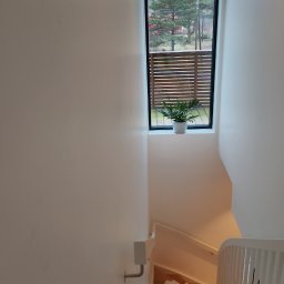Szwagier usługi remontowo ,wykonczenowe - Jasne wnętrze: schody zabezpieczone folią malarską, białe ściany, okno z widokiem na zieleń. Minimalistyczny design, świeżo po malowaniu.