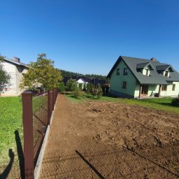 MT OGRODZENIA Maciej Tokarczyk - Nowoczesne ogrodzenie panelowe w kolorze brązowym, z widocznymi słupkami i podmurówką, na tle zielonego trawnika i domów jednorodzinnych w słoneczny dzień.