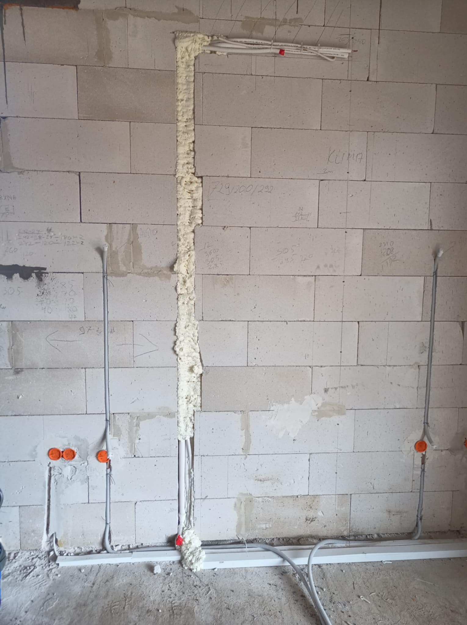 Instalacja elektryczna w trakcie prac w Olsztynie: kable w ścianie zabezpieczone pianką montażową, puszki elektryczne zamontowane, widoczne przewody. Surowy stan.