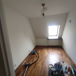 Eduard Ustymov - Pokój na poddaszu po malowaniu ścian na biało, z drewnianą podłogą, oknem dachowym, widocznym odkurzaczem i wiaderkami z farbą oraz innymi materiałami malarskimi.