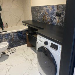 Eduard Ustymov - Wykończona łazienka z pralką Samsung, białą armaturą i marmurowymi płytkami na ścianach i podłodze, widoczne czarne blaty i ciemnoniebieskie płytki dekoracyjne.