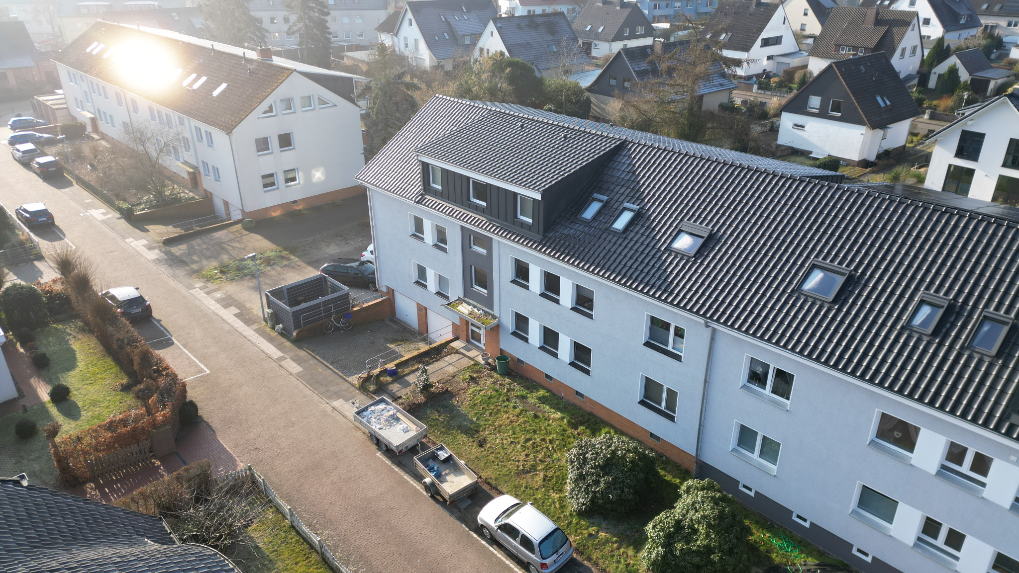 Widok z góry na budynek wielorodzinny z nowym, ciemnoszarym dachem z dachówki ceramicznej i oknami dachowymi, widoczne przyczepki na ulicy.