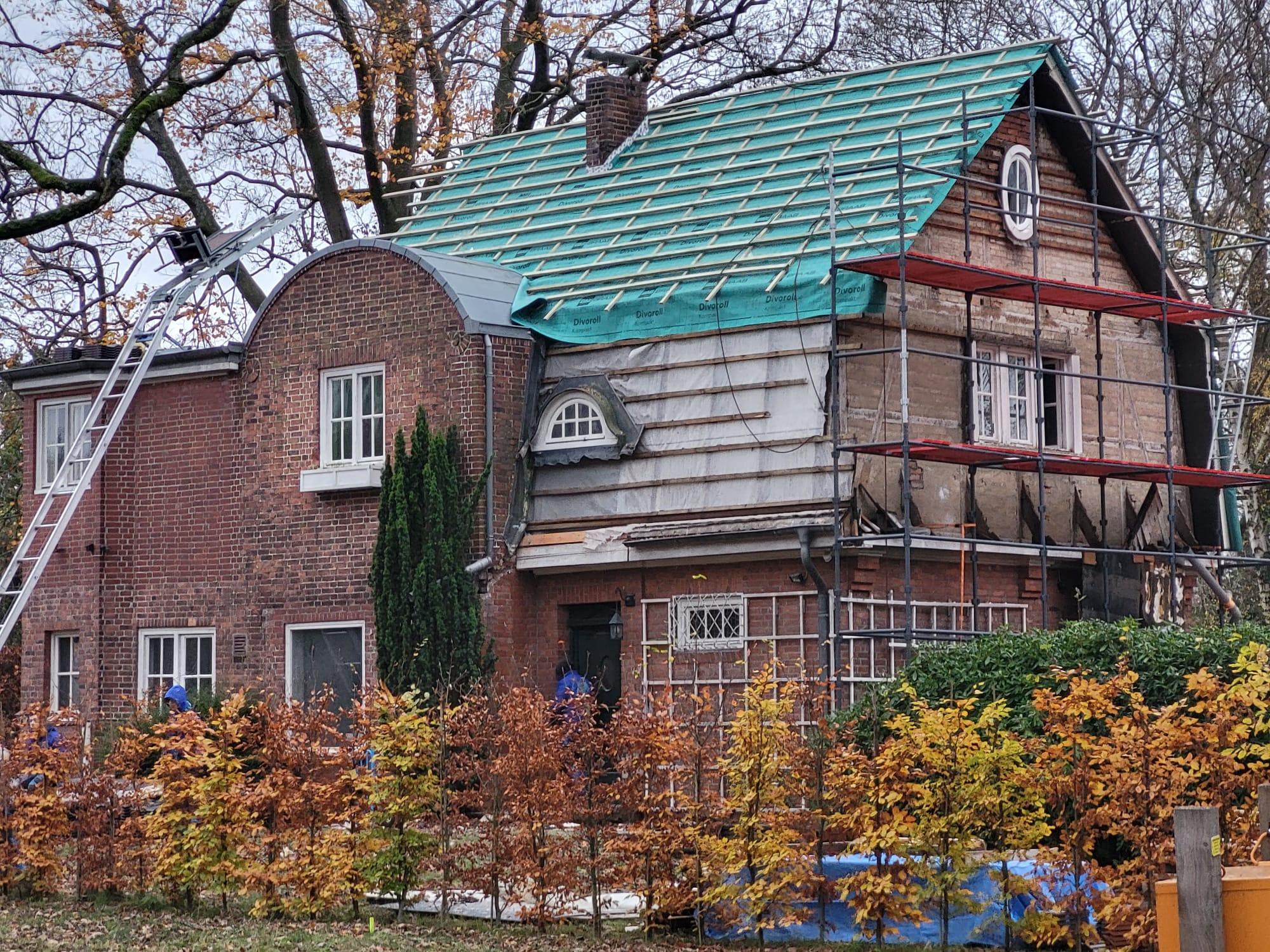 Dom w Poznaniu w trakcie prac dekarskich; widoczne rusztowania, częściowo zdjęte poszycie i nowa membrana dachowa w kolorze zielonym.