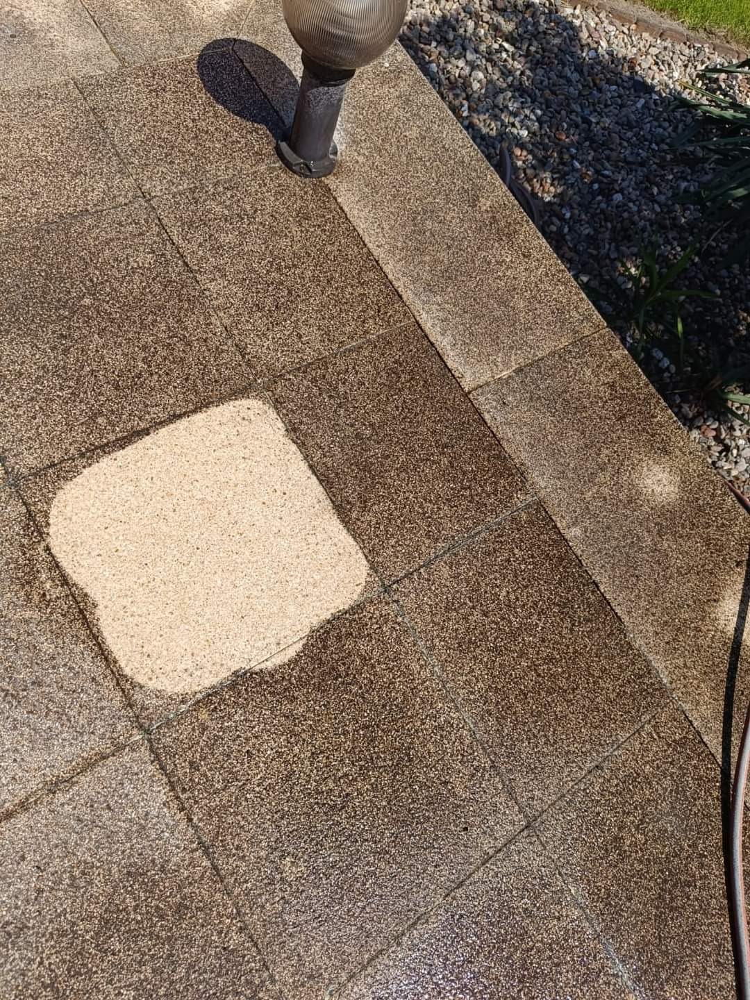 Fragment kostki brukowej częściowo wyczyszczonej, z widoczną różnicą w kolorze i zabrudzeniu między czystą a brudną powierzchnią, obok lampa ogrodowa i fragment węża.