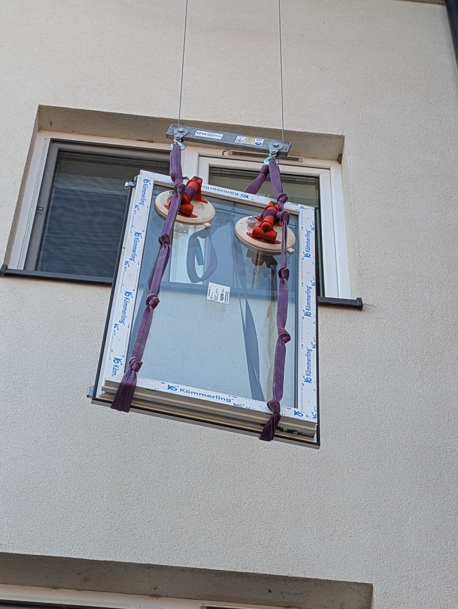 Montaż okna PCV na elewacji budynku za pomocą specjalistycznego sprzętu z przyssawkami. Widoczne okno marki Kömmerling.