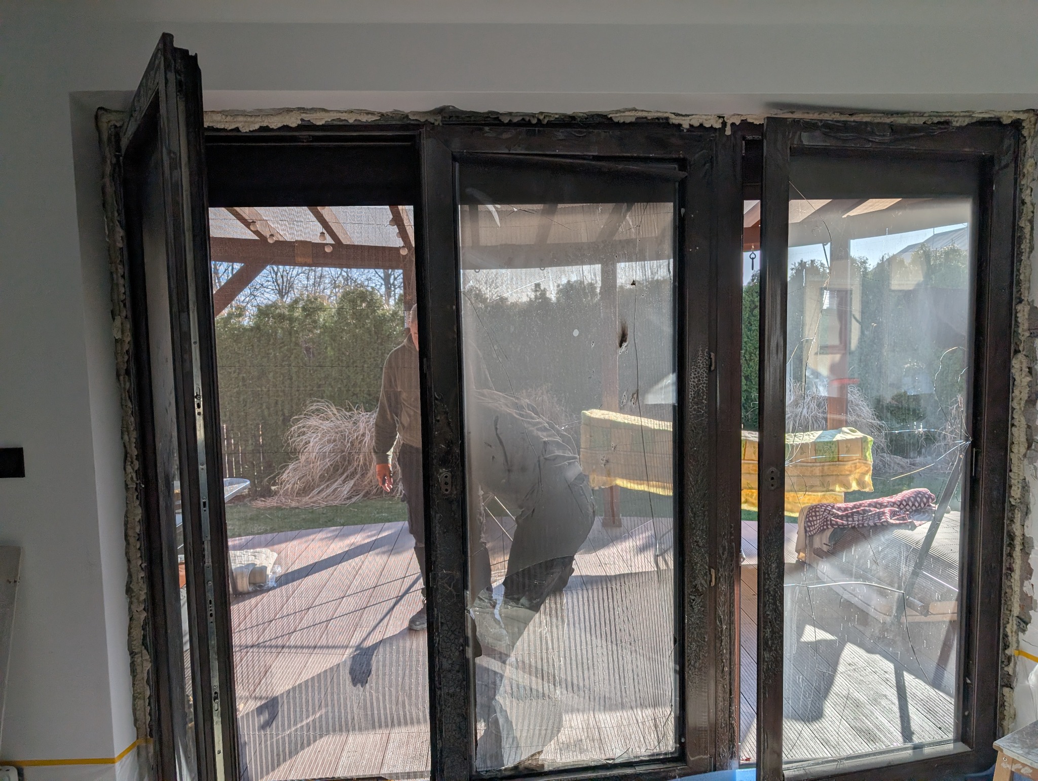 Demontaż starej stolarki okiennej z uszkodzonymi szybami. Widoczne ślady pianki montażowej i przygotowania do instalacji nowych okien.
