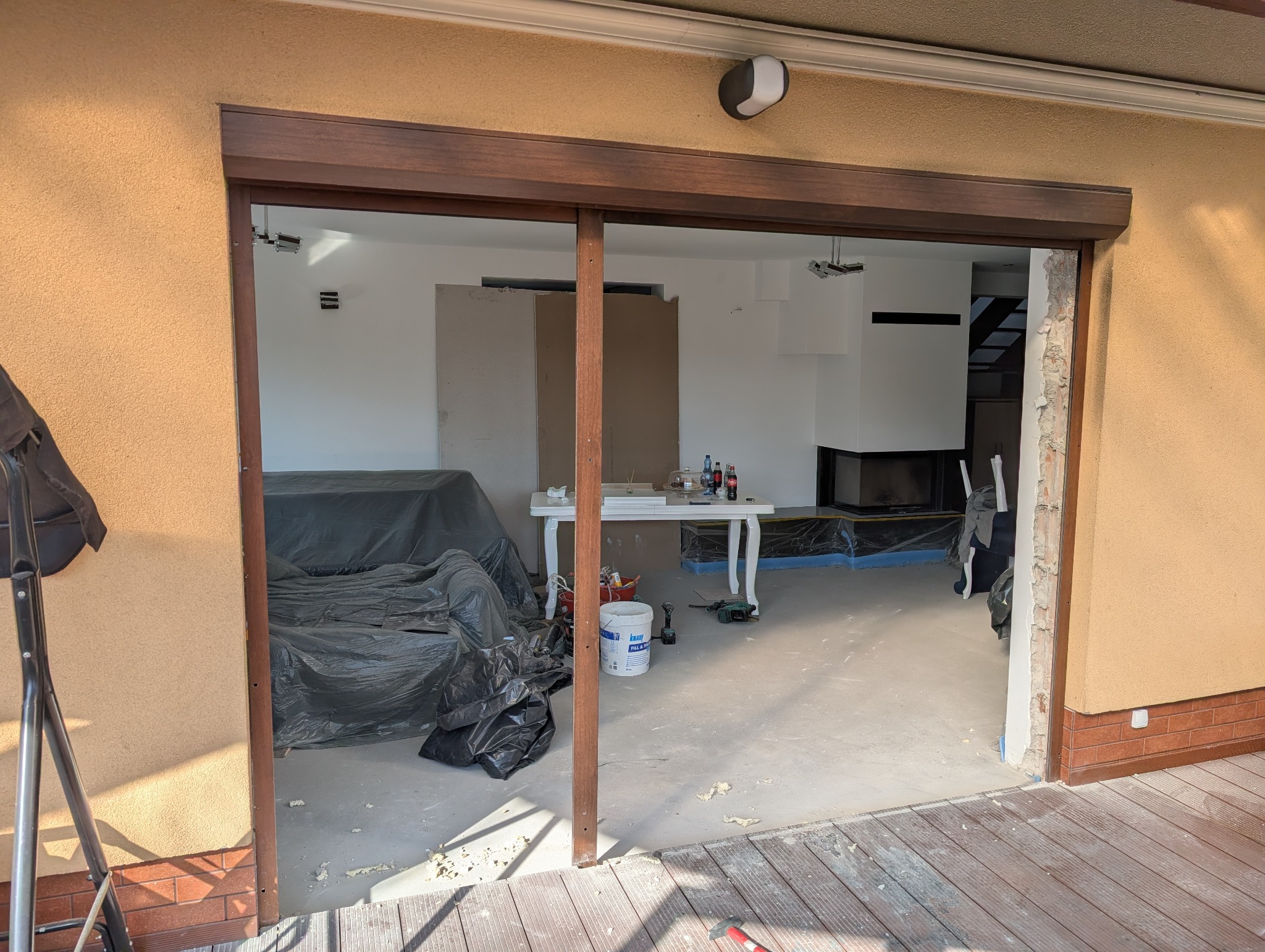 Montaż brązowych drzwi przesuwnych balkonowych. Widoczne narzędzia i materiały budowlane wewnątrz pomieszczenia. Częściowo odsłonięta ściana.