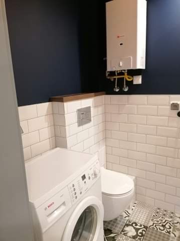 Wykończona łazienka z białą pralką Bosch, podwieszaną toaletą, białymi płytkami typu metro i wzorzystą podłogą. Na ścianie zamontowany piec gazowy.