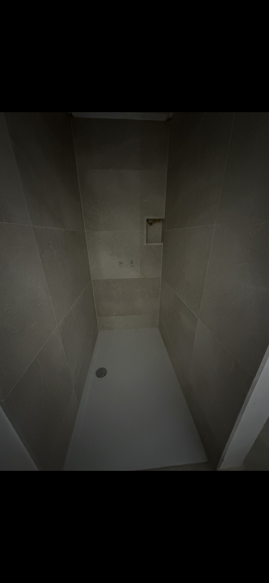 Wykończony brodzik z odpływem liniowym i szarą, matową okładziną ścienną z wnęką na kosmetyki. Minimalistyczny design kabiny prysznicowej.