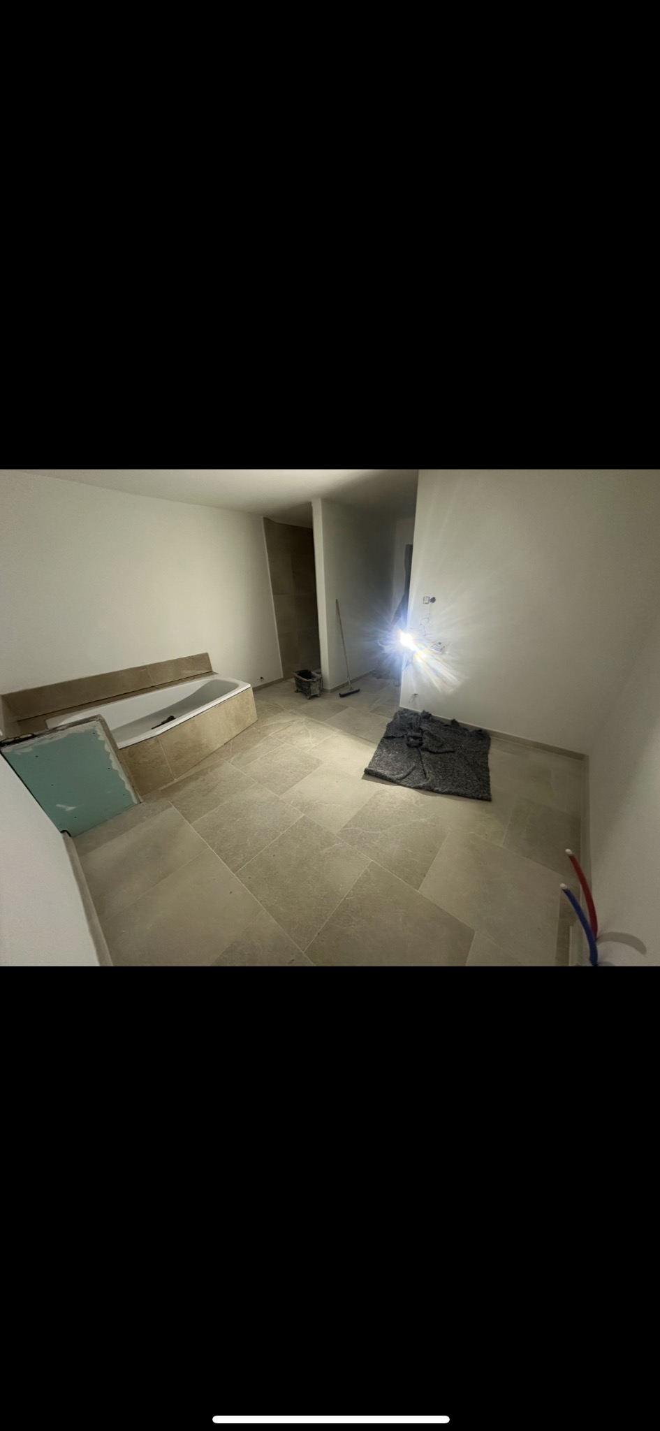 Jasne, beżowe płytki podłogowe w łazience po remoncie. Częściowo obudowana wanna, widoczne narzędzia i materiały budowlane. Świeże, minimalistyczne wykończenie.