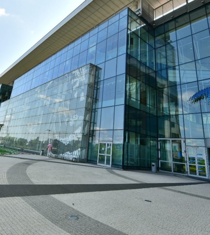 Nowoczesny, przeszklony budynek biurowy z widoczną osobą w oddali i dekoracyjnym wzorem na jednej ze szklanych ścian.