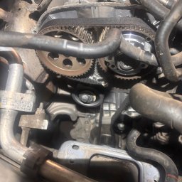 KK Performance JAKUB KOŹBIAŁ - Widok z bliska na silnik samochodowy z widocznym paskiem rozrządu, kołami zębatymi i przewodami, ukazujący etap naprawy lub konserwacji.