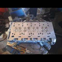 Głowica silnika po obróbce, widoczne nowe gniazda zaworowe, obok leżą narzędzia warsztatowe.