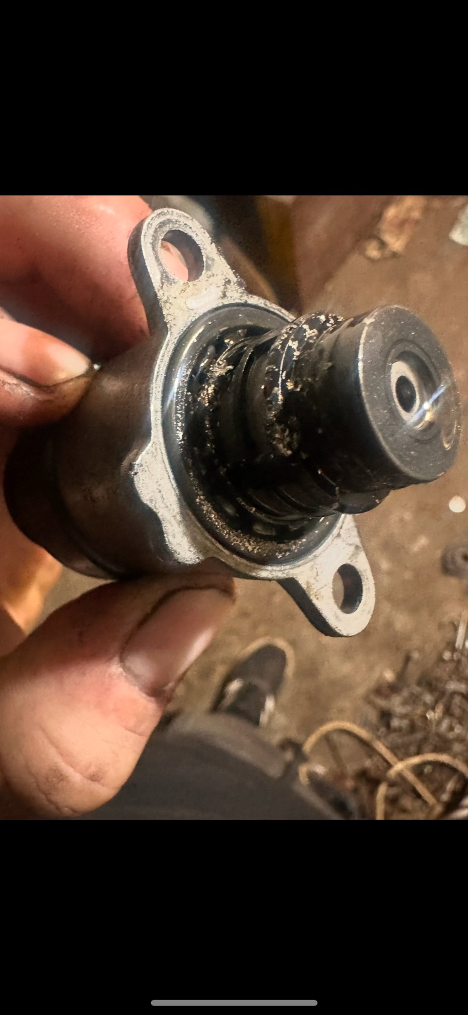 Brudny, metalowy element samochodowy trzymany w dłoni, widoczne ślady zużycia i zanieczyszczenia.