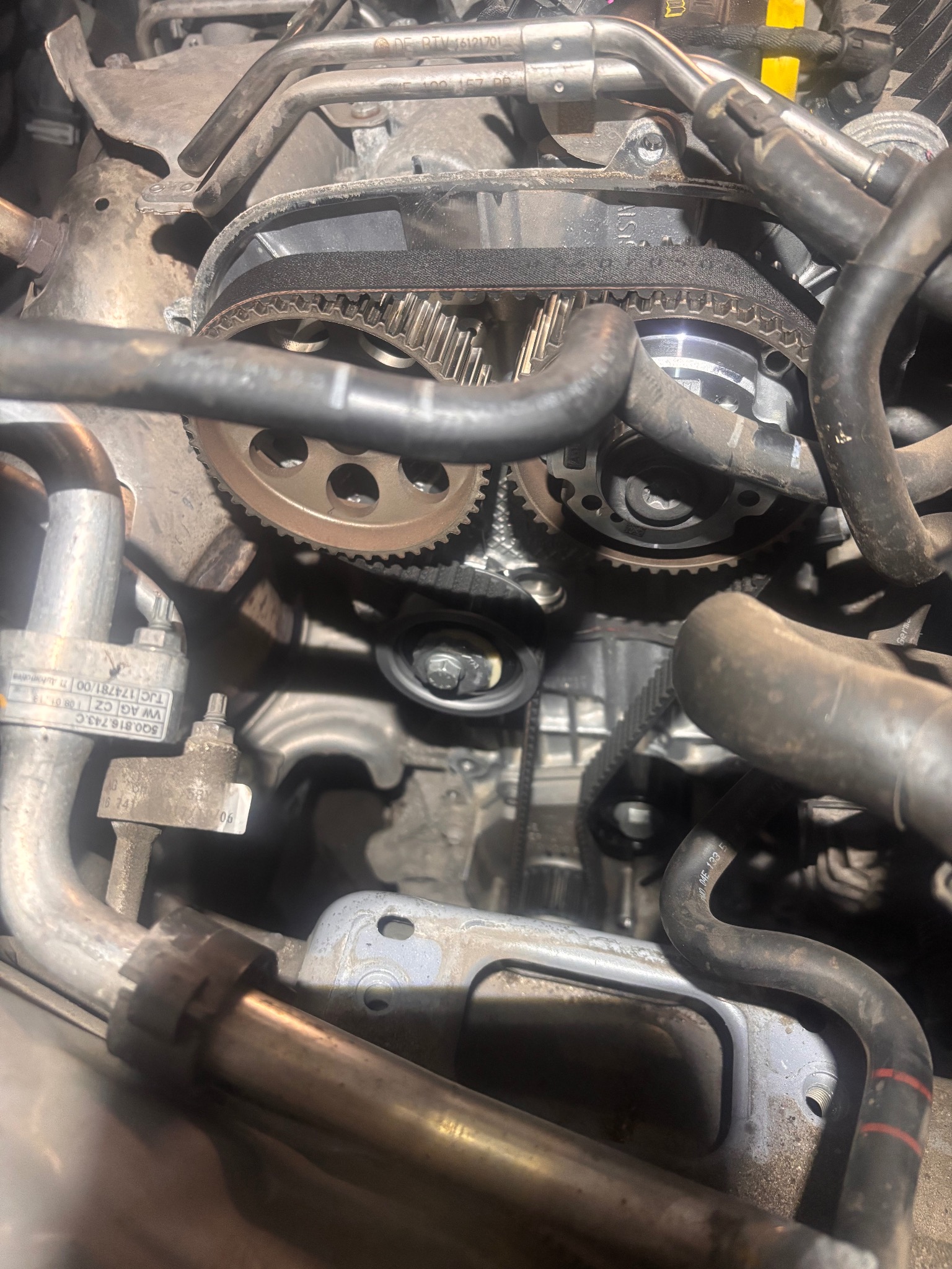 Widok z bliska na silnik samochodowy z widocznym paskiem rozrządu, kołami zębatymi i przewodami, ukazujący etap naprawy lub konserwacji.