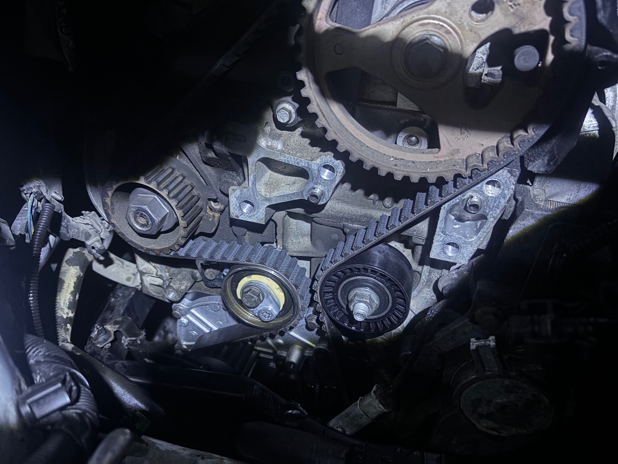 Otwarty silnik samochodowy z widocznym paskiem rozrządu i zębatkami w trakcie naprawy, oświetlony punktowo.