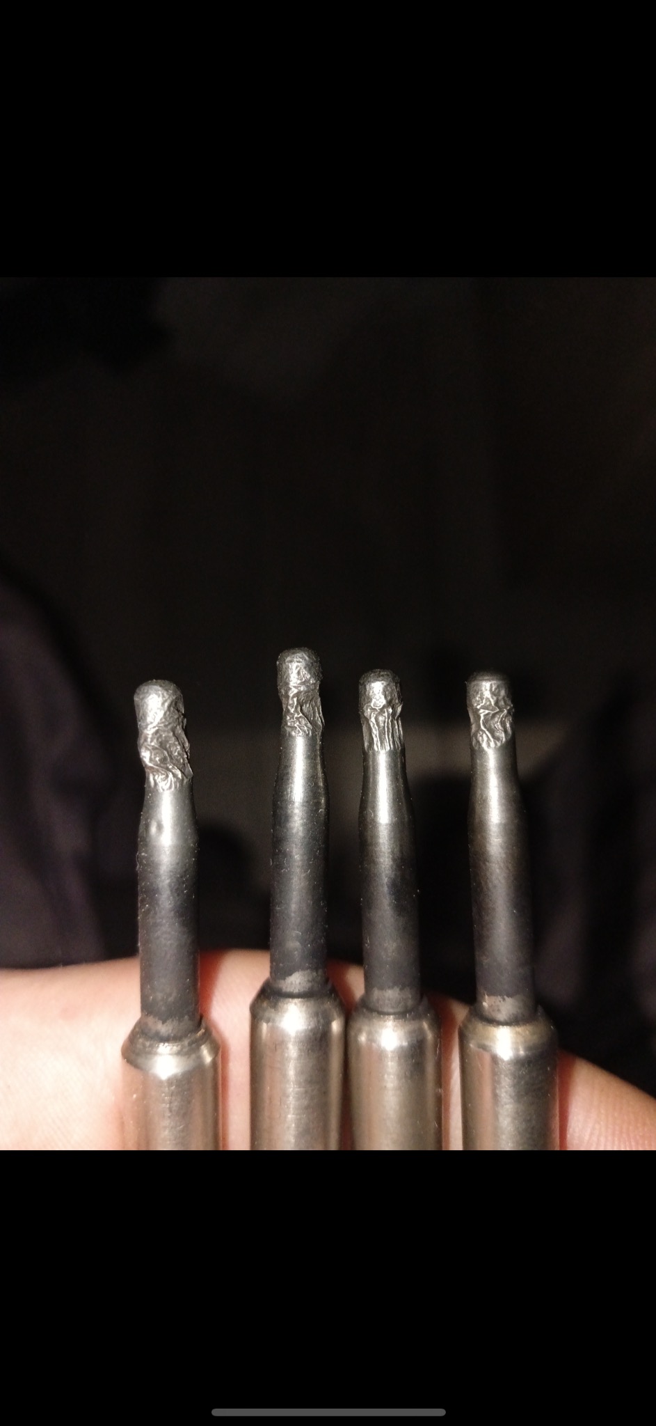 Zużyte świece żarowe diesla z wyraźnymi śladami eksploatacji i uszkodzeń na końcówkach grzejnych, trzymane w dłoni na ciemnym tle.
