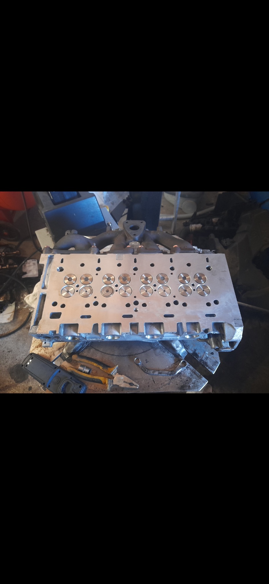 Głowica silnika po obróbce, widoczne nowe gniazda zaworowe, obok leżą narzędzia warsztatowe.