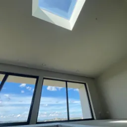 Jasne wnętrze z oknami i świetlikiem, świeżo po gładziowaniu ścian i sufitu. Widok na błękitne niebo i panoramę miasta. Minimalistyczny design.