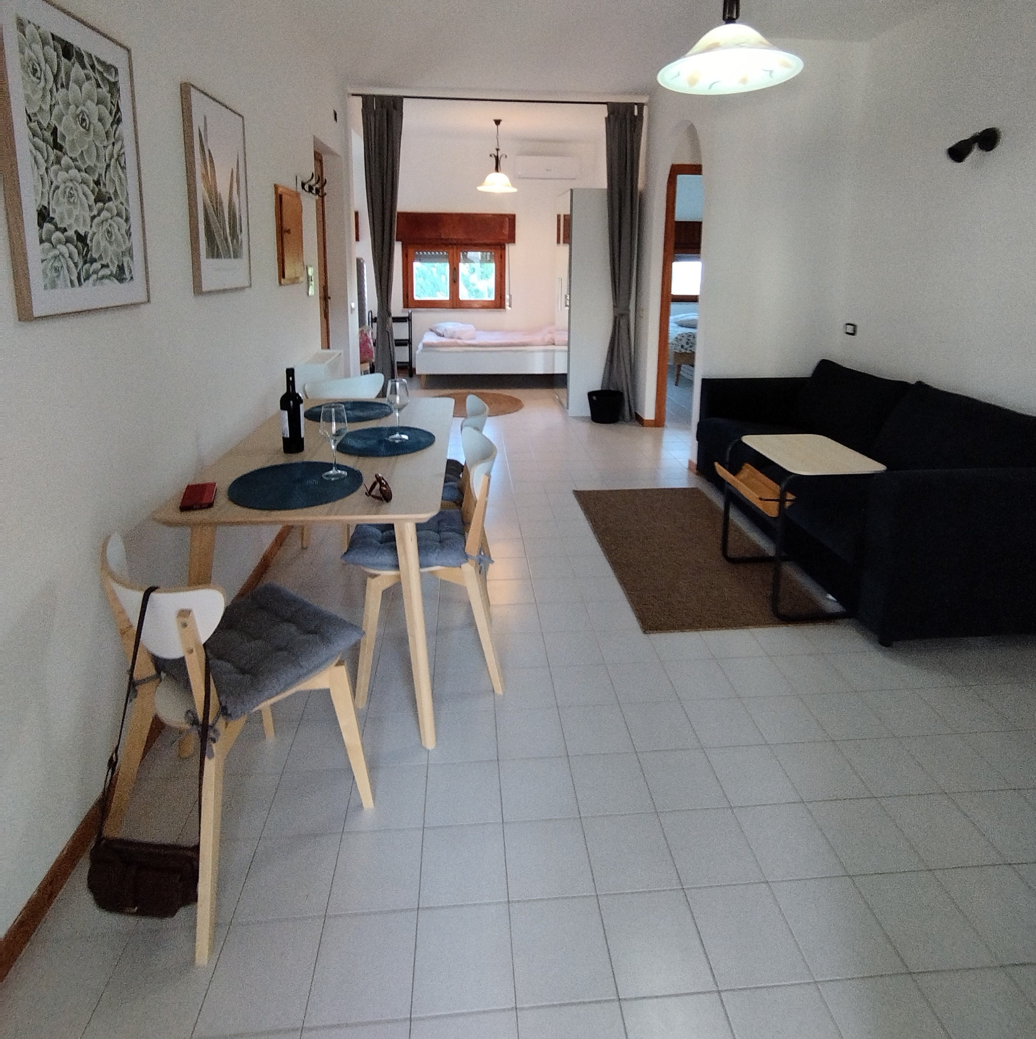 Jasne wnętrze mieszkania z jadalnią, salonem i widokiem na sypialnię przez otwarte przejście; na ścianach wiszą obrazy z motywami roślinnymi.